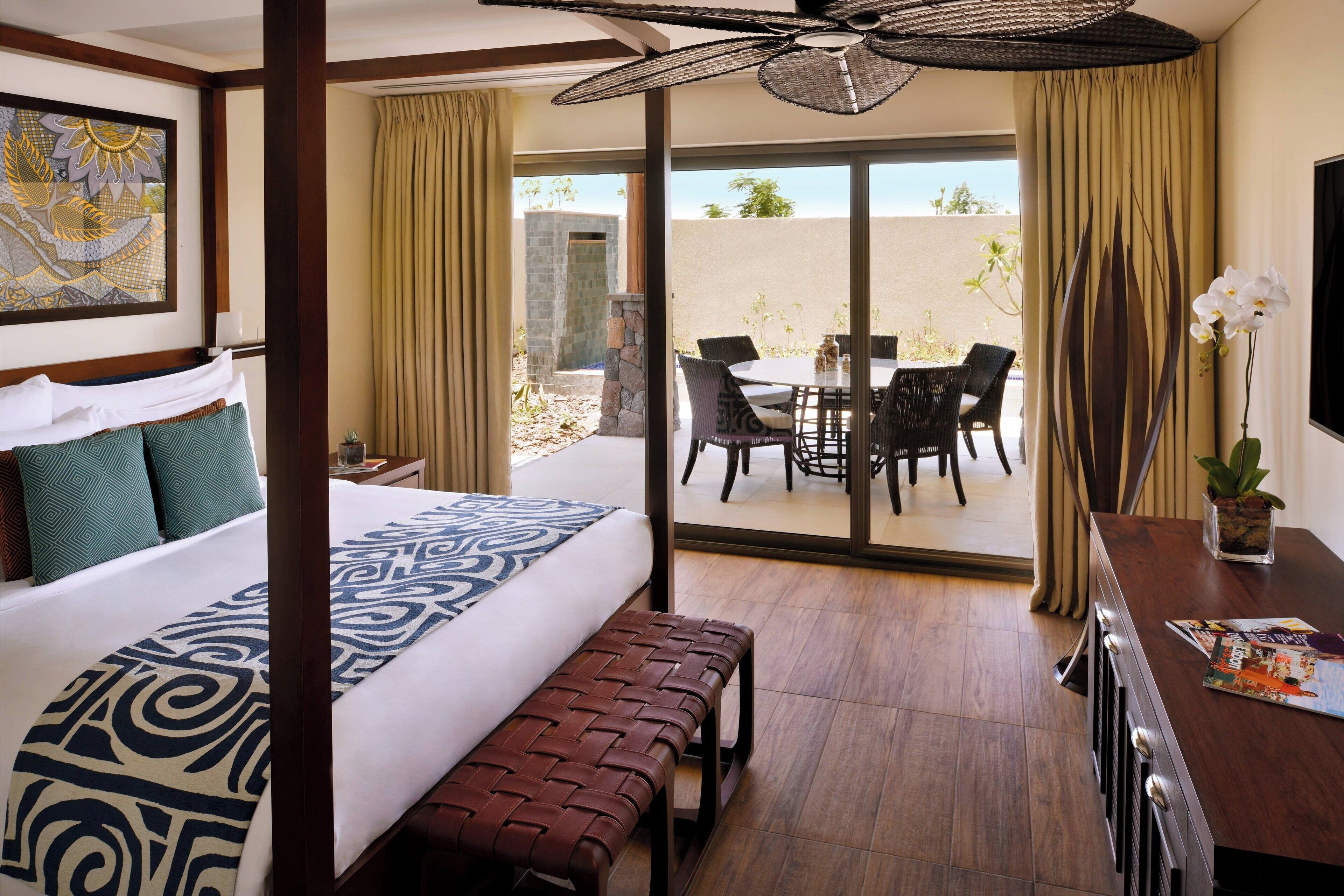 A hotel room with a large bed, a bench, a dining table with chairs, and a view of the outdoors.