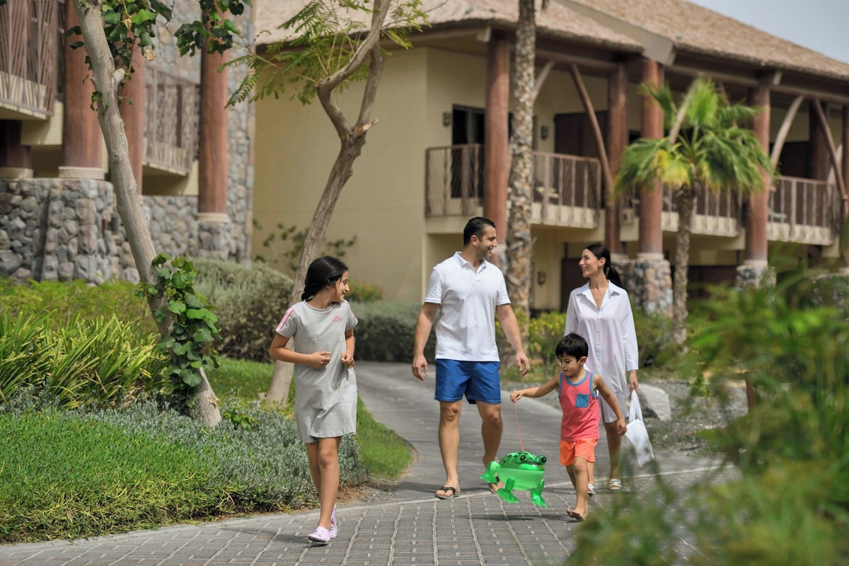 A family walking on a paved path with a building featuring stone columns and balconies in the background.