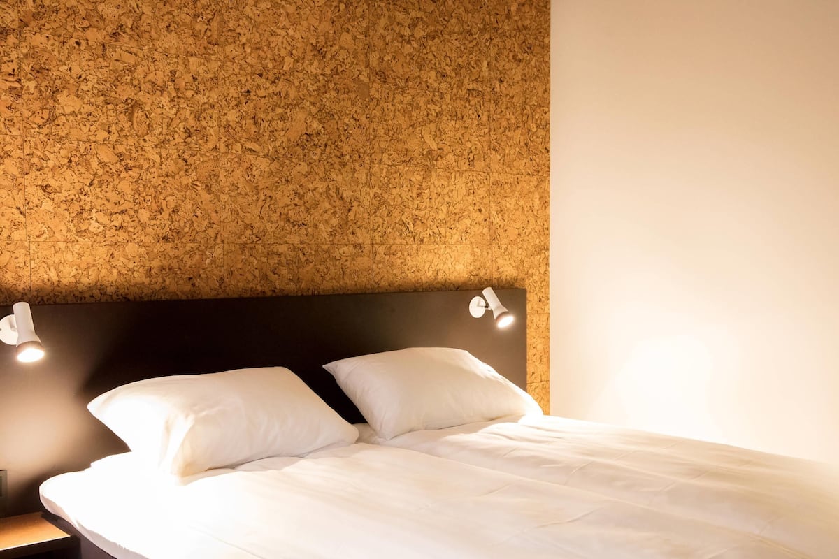 Un lit bien fait, avec du linge de lit blanc, une tête de lit sombre et deux lampes de chevet.