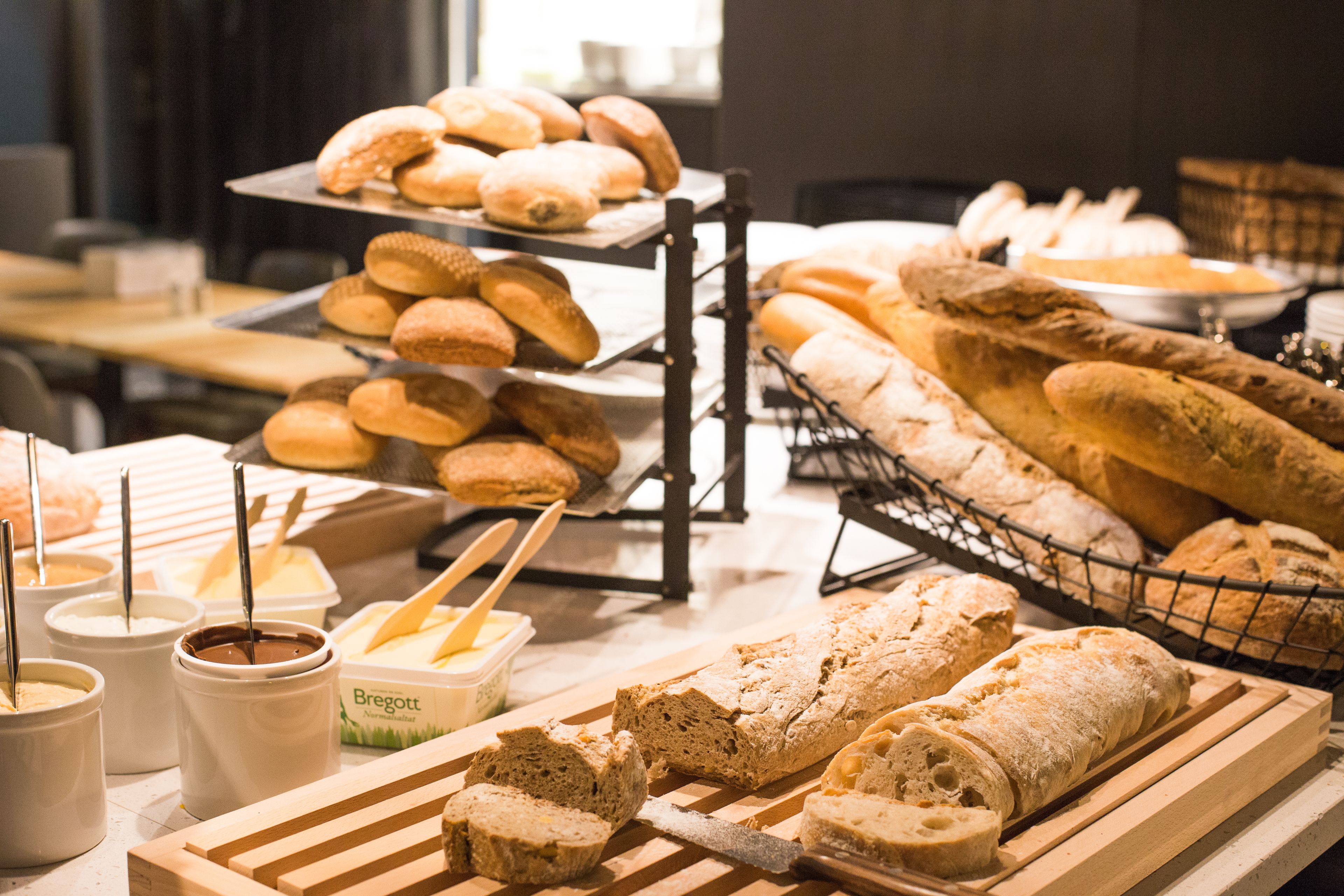 A variety of breads and pastries on display, including baguettes and rolls, with containers of spreads and butter.