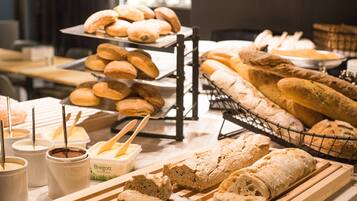 A variety of breads and pastries on display, including baguettes and rolls, with containers of spreads and butter.