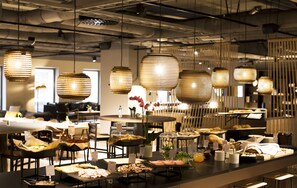 A modern dining area with hanging pendant lights, a buffet setup with various food items, and a contemporary interior design. - Comfort Hotel Kista (Kista)
