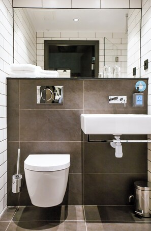 A modern bathroom with a white toilet, a sink, and a trash can. - Comfort Hotel Kista (Kista)