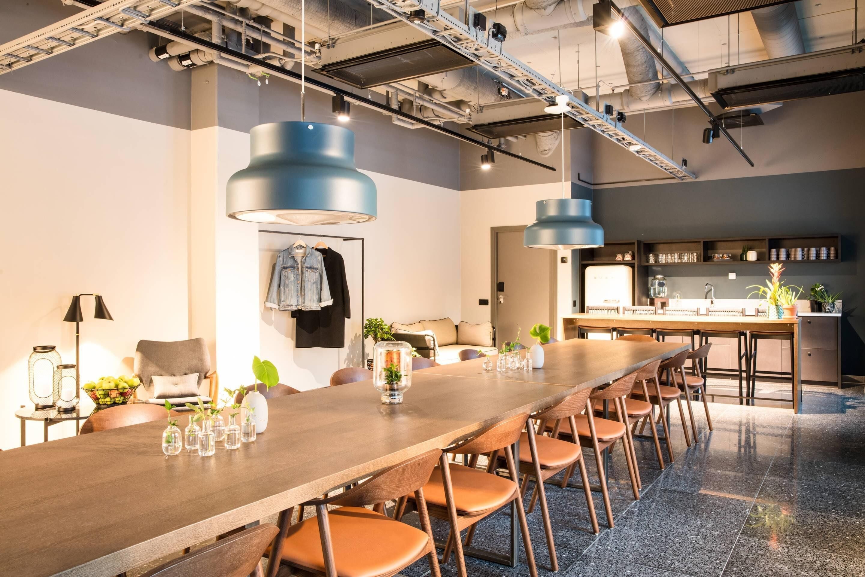 A modern conference room with a long wooden table, multiple chairs, and pendant lighting.