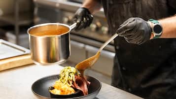 Una persona con uniforme y guantes sirve comida desde una olla a un plato.