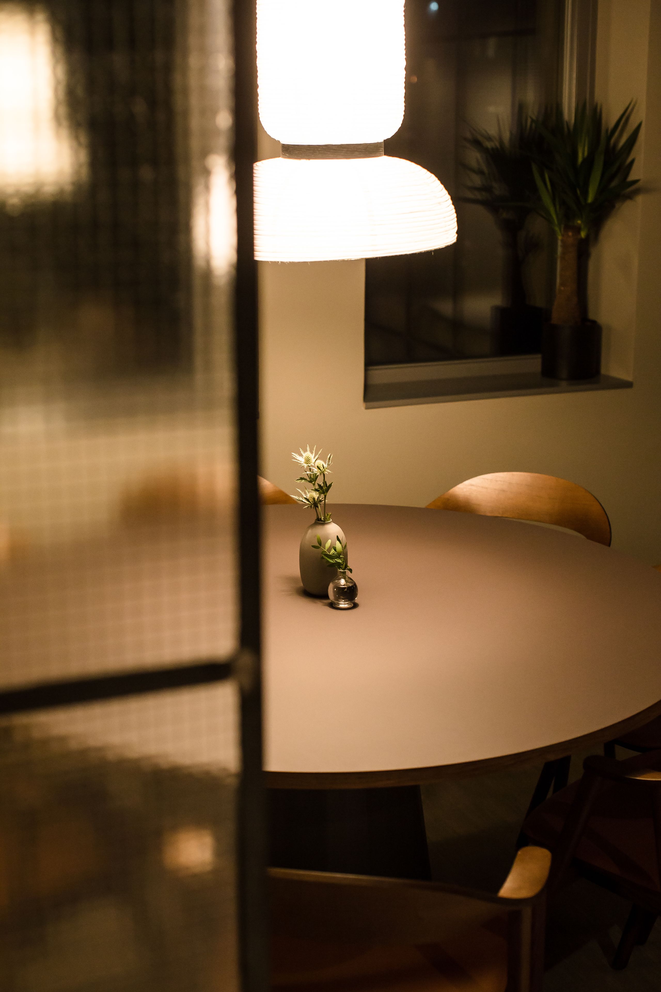 Une table de salle à manger ronde, ornée d’un vase de fleurs, d’une lampe et de chaises.