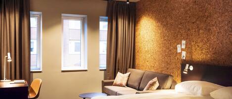 Una habitación de hotel moderna con una cama grande, un sofá, un escritorio y dos ventanas.
