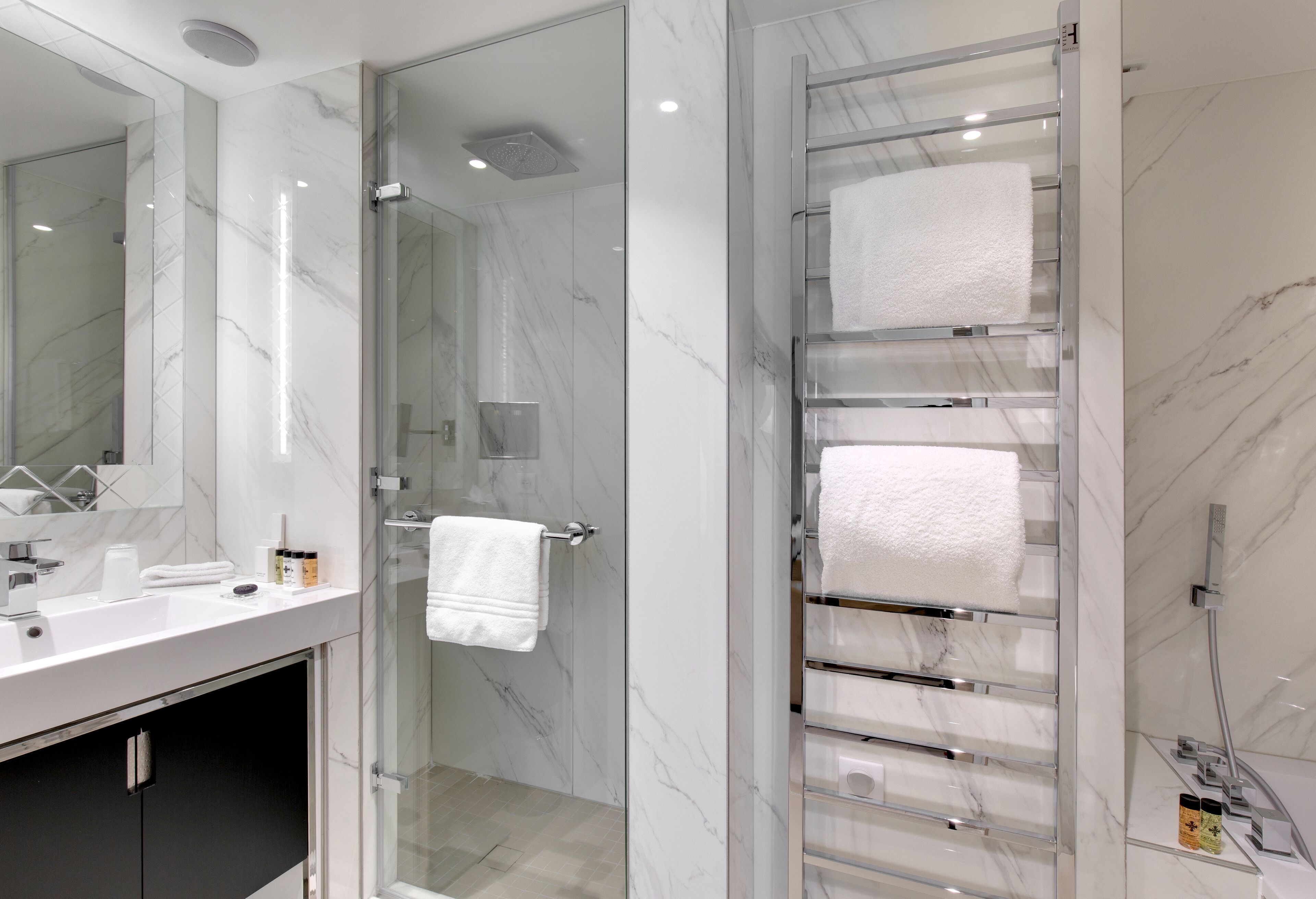 A modern bathroom with a glass shower enclosure, a white marble sink, and a towel rack with multiple towels.