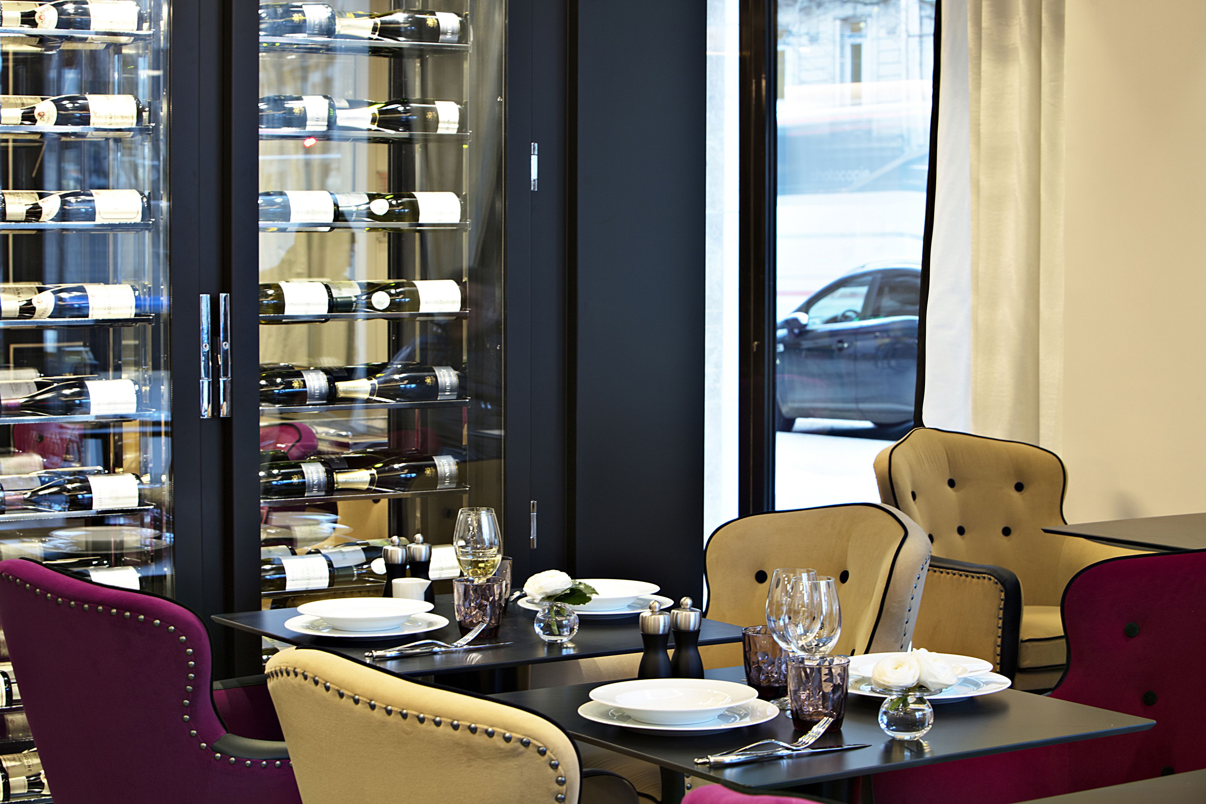 A dining area with a glass wine rack, neatly set tables, and comfortable seating.