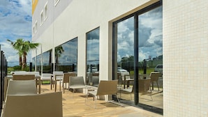 An outdoor seating area with chairs and tables, large windows, and a view of the sky and clouds. - ibis Styles Birigui (Birigui)