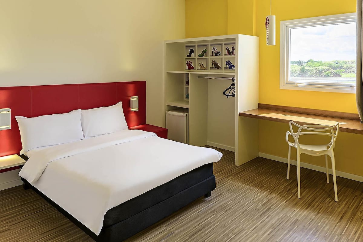 Habitación de hotel con cama, escritorio, silla, armario y ventana con vistas.
