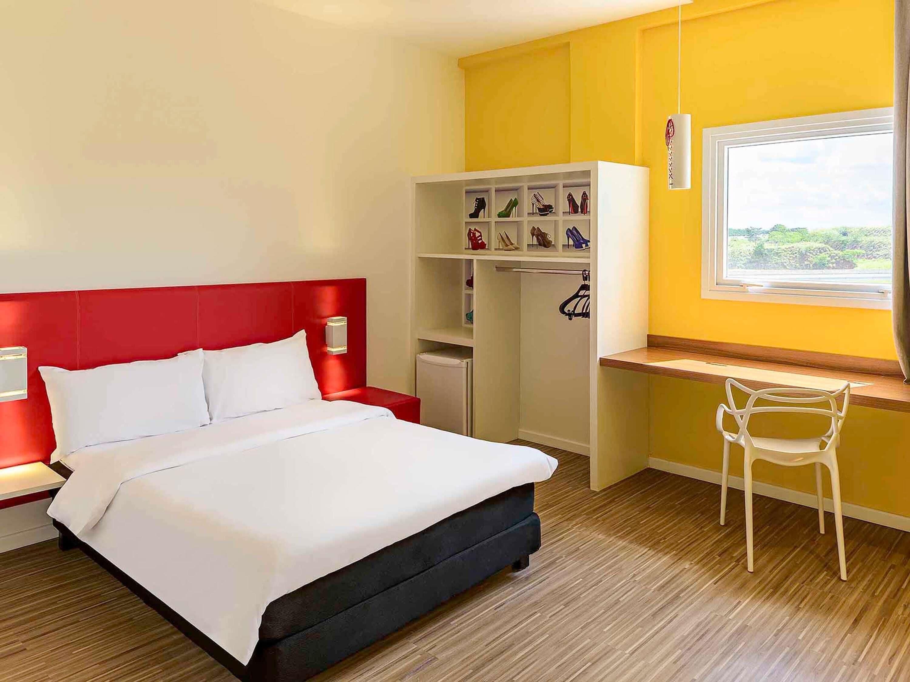 Habitación de hotel con cama, escritorio, silla, armario y ventana con vistas.