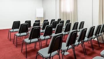 A conference room with rows of foldable chairs, a whiteboard, and a red carpeted floor.