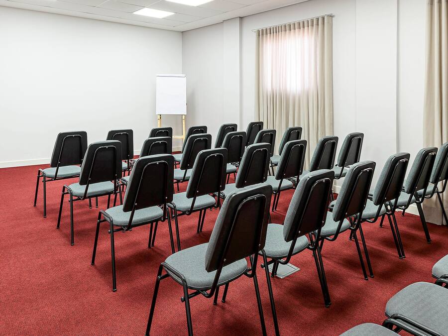 A conference room with rows of foldable chairs, a whiteboard, and a red carpeted floor.