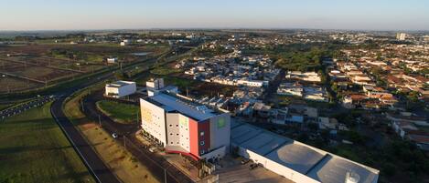 Vista aérea de uma grande instalação industrial com ampla área de estacionamento, cercada por edifícios residenciais e comerciais.
