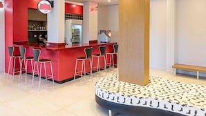 A modern bar area with red accents, a central column, and a circular seating arrangement around a shoe display. - ibis Styles Birigui (Birigui)