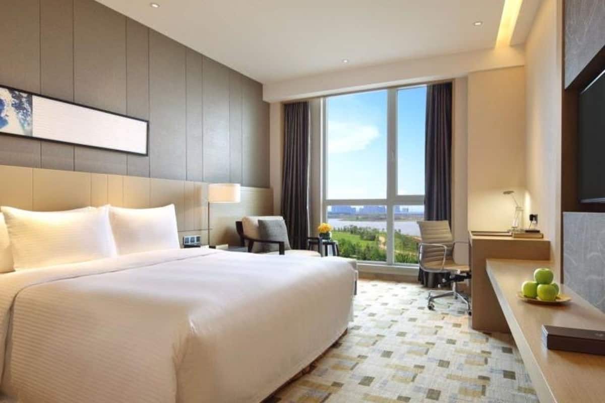 A hotel room with a large bed, a desk, a chair, and a view of the city through the window.