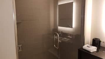 Un baño moderno con cabina de ducha de vidrio, encimera oscura y espejo.