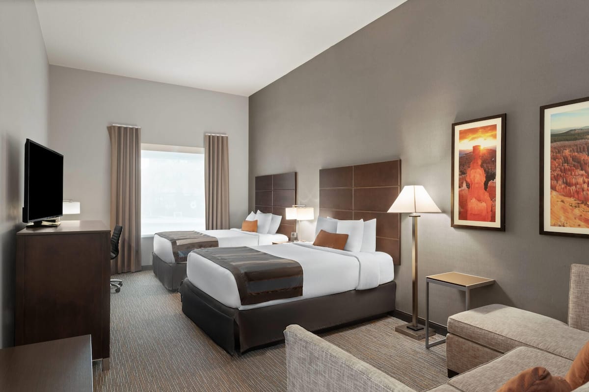 A hotel room with two beds, a desk, a chair, a TV, and artwork on the walls.