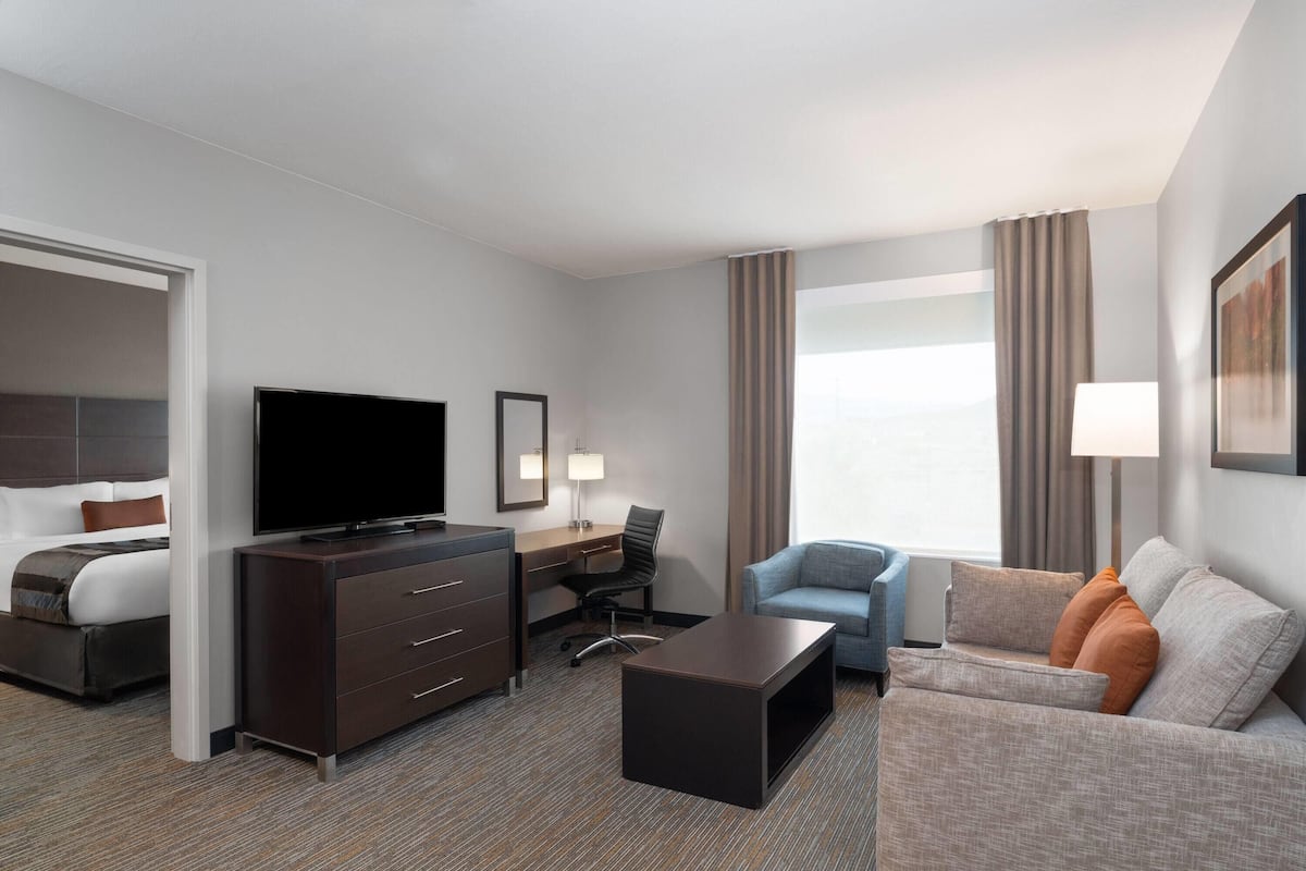 A hotel room with a bed, a desk with a computer, a television, a sofa, and a window with curtains.