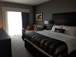 Una habitación de hotel con una cama grande, un sofá, un escritorio y una ventana con cortinas.