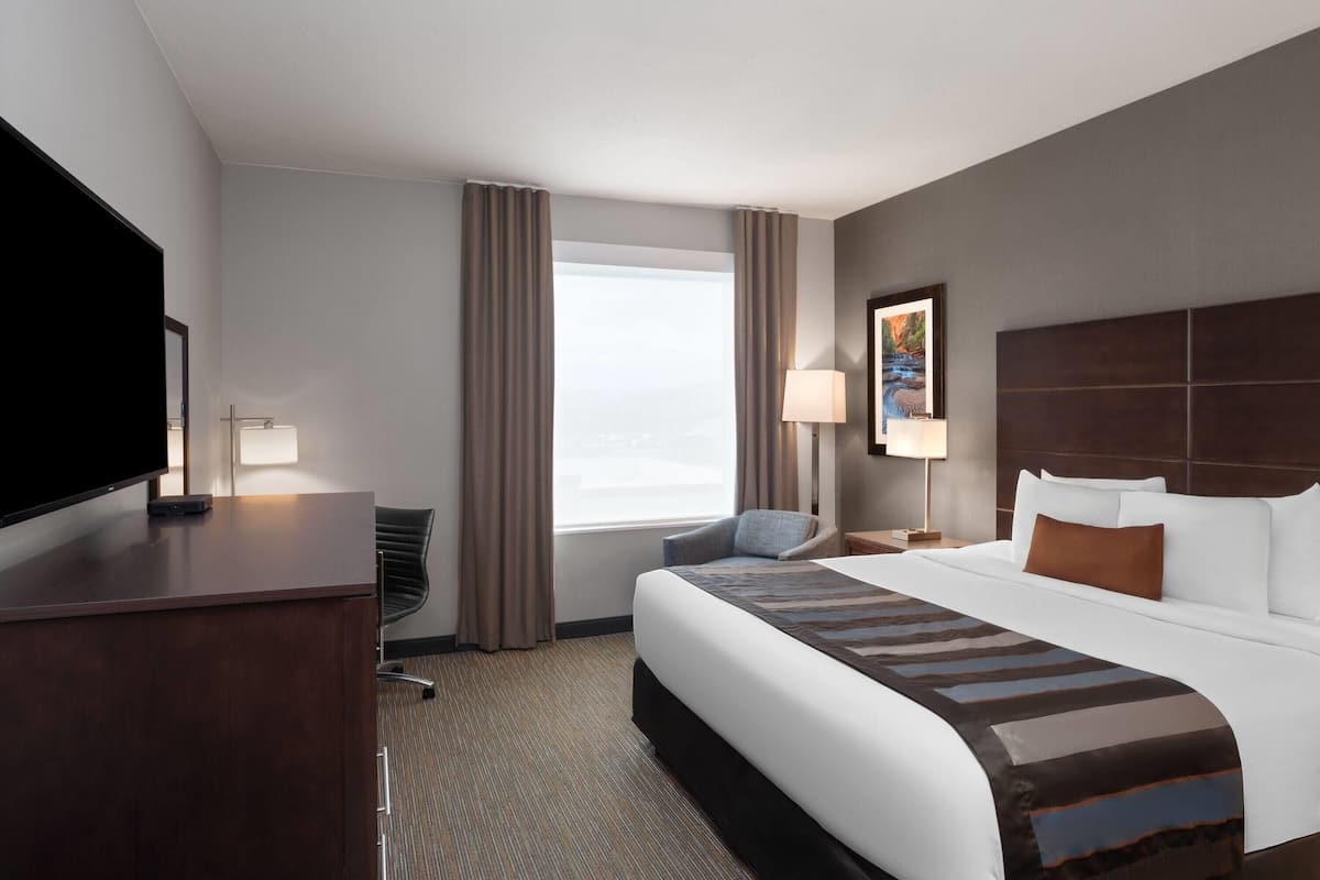 A hotel room with a large bed, a desk, a chair, a television, and a window with curtains.
