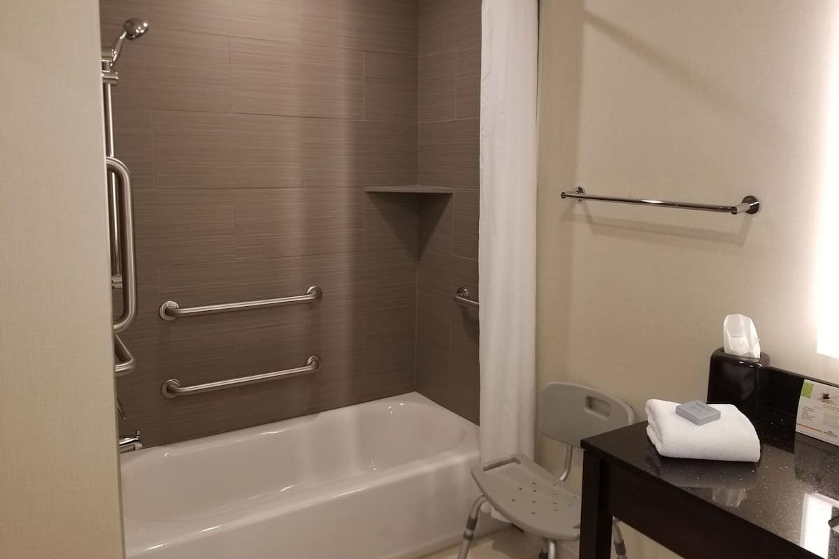 Een badkamer met een inloopdouche, handgrepen, een handdoekrek en een stoel.