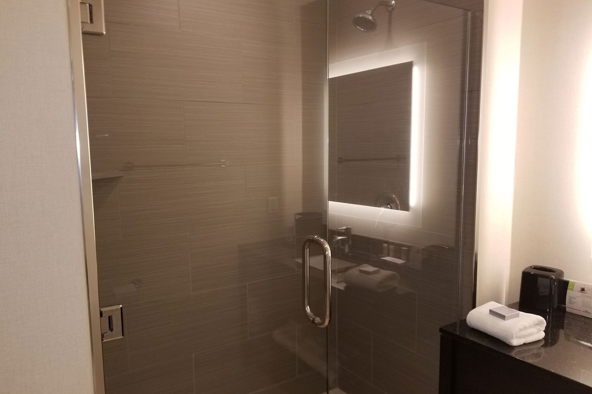 Un baño moderno con cabina de ducha de vidrio, encimera oscura y una toalla en el lavamanos.