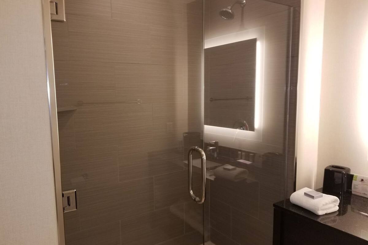 A modern bathroom with a glass shower enclosure, a dark countertop, and a towel on the sink.