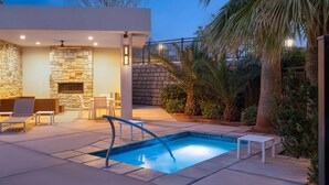 A modern outdoor pool area with stone walls, a built-in fireplace, and outdoor seating.