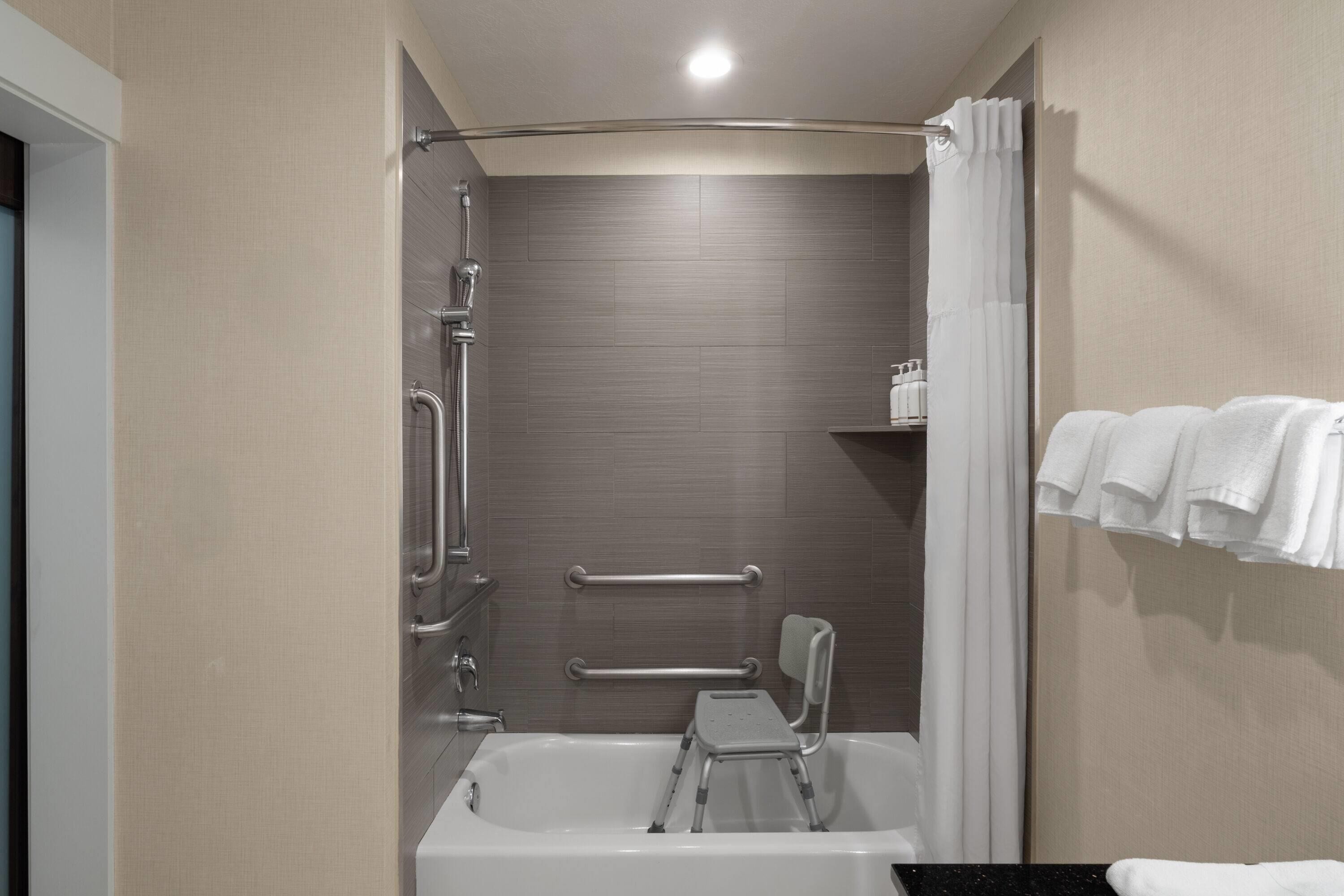 Une salle de bain moderne équipée d’une baignoire, d’une douche et de barres d’appui.