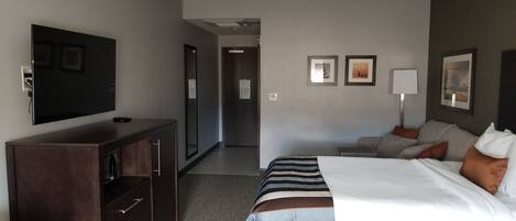 A hotel room with a large bed, a TV, a dresser, and a desk.