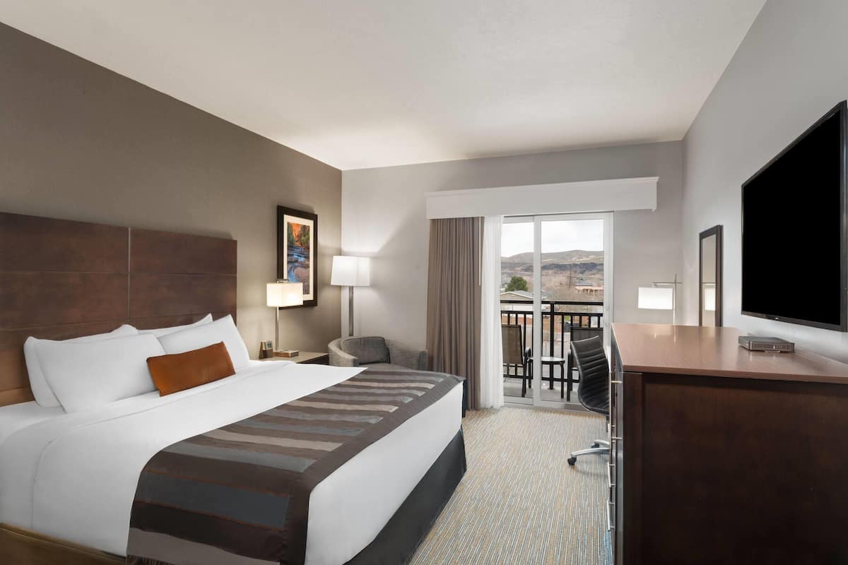 A hotel room with a large bed, a desk, a TV, and a balcony with a view.