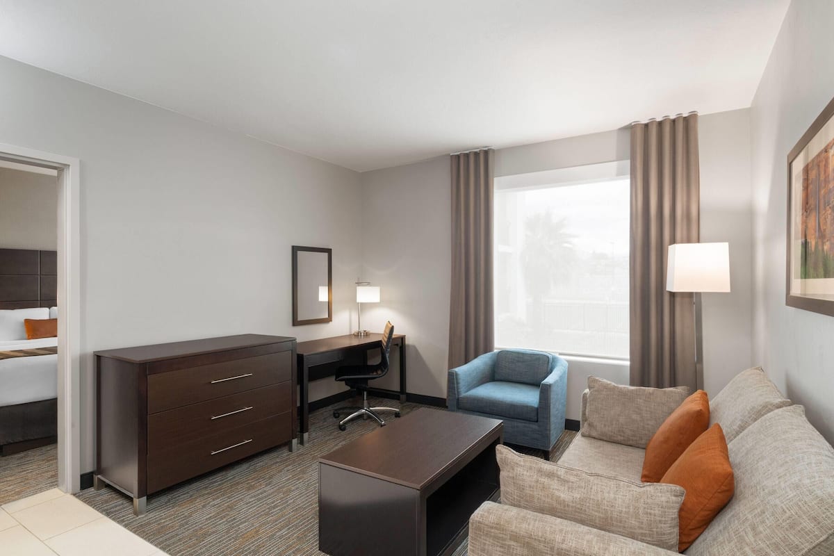 A hotel room with a bed, a desk, a chair, a sofa, and a large window with curtains.