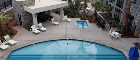 Una piscina con sillas de descanso y un área de estar techada, rodeada de un jardín ajardinado y un edificio de piedra.