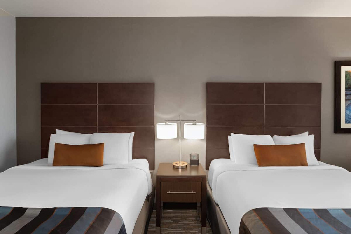 A hotel room with two beds, a nightstand with a lamp, and a framed picture on the wall.