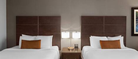 A hotel room with two beds, a nightstand with a lamp, and a framed picture on the wall.