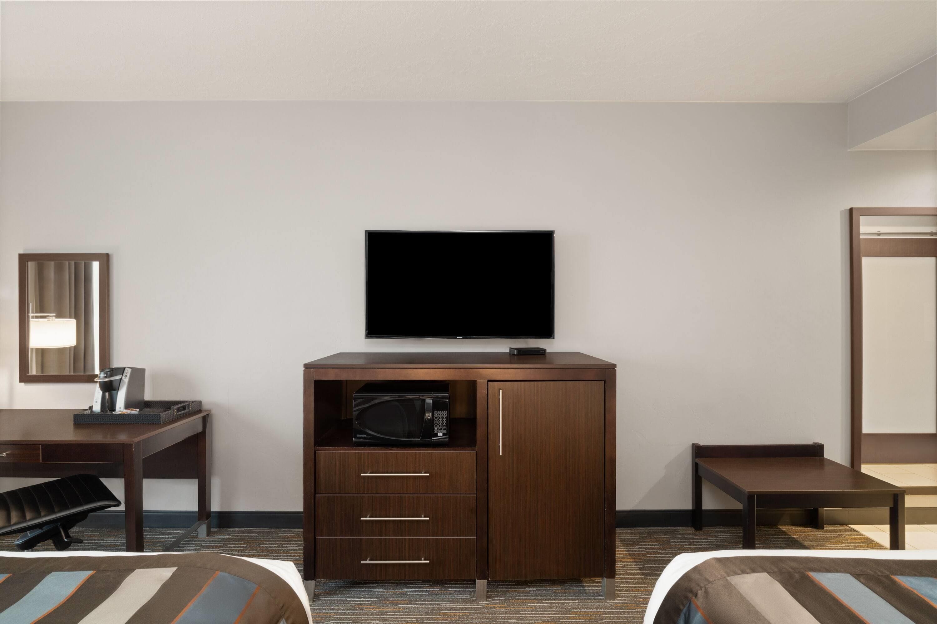 Una habitación de hotel con cama, escritorio, minibar, televisor y espejo.