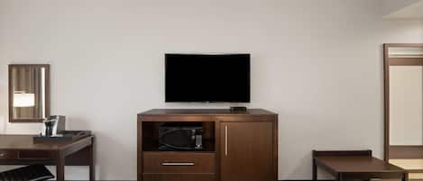 Una habitación de hotel con cama, escritorio, minibar, televisor y espejo.