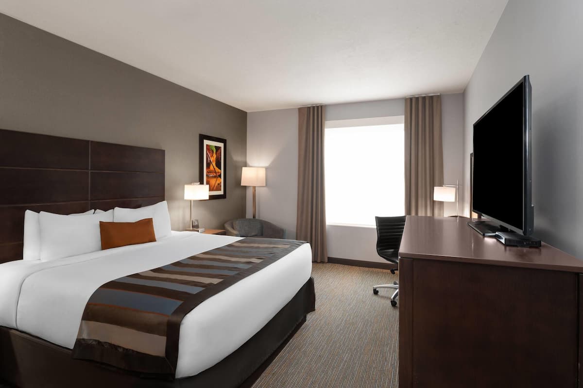 A hotel room with a large bed, a flat-screen TV, a desk, and a window with curtains.