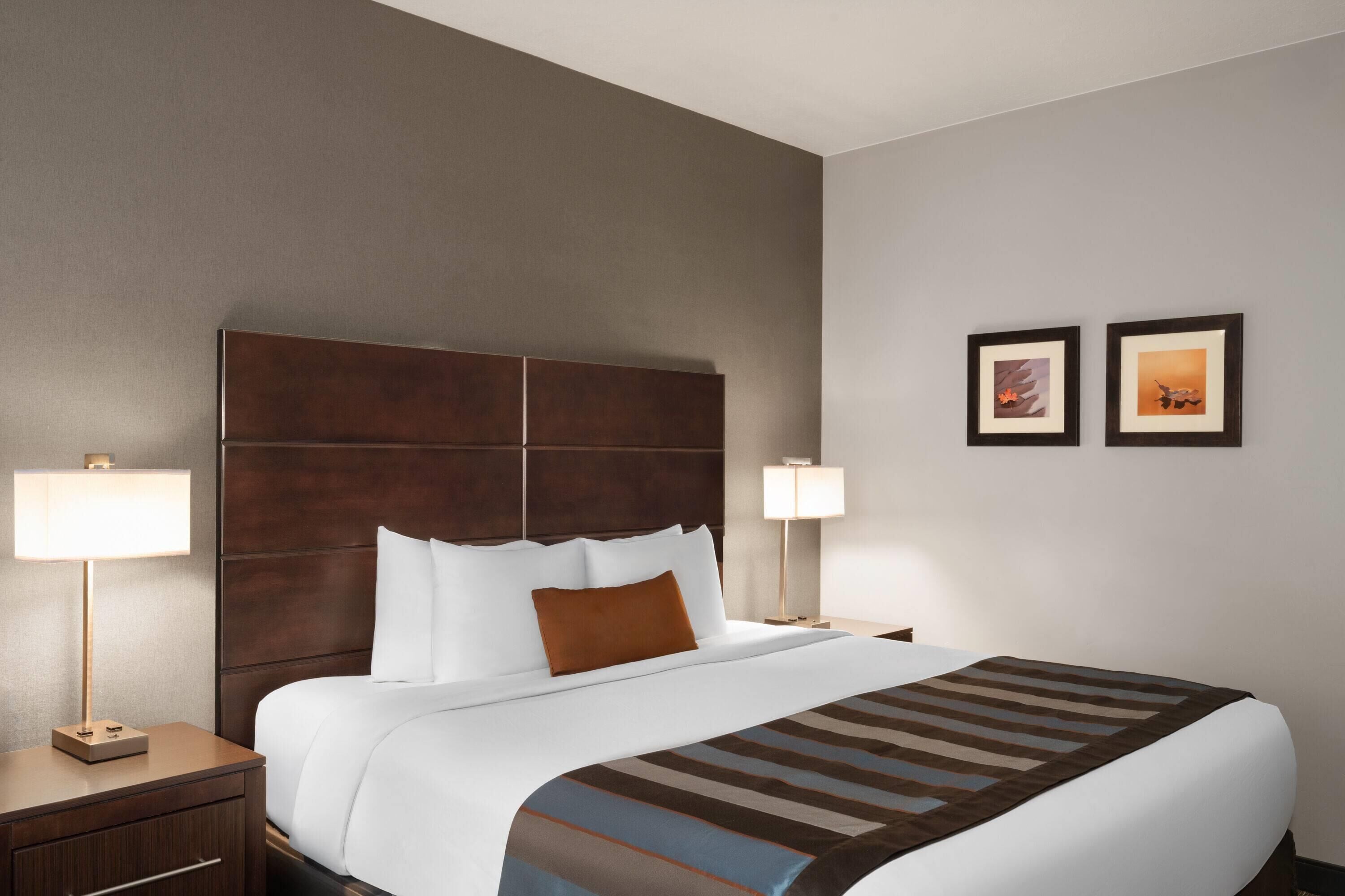 A hotel room with a large bed, two bedside tables, a headboard, and two wall-mounted lamps.
