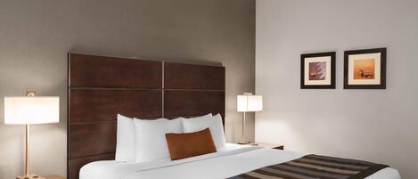 A hotel room with a large bed, two bedside tables, a headboard, and two wall-mounted lamps.