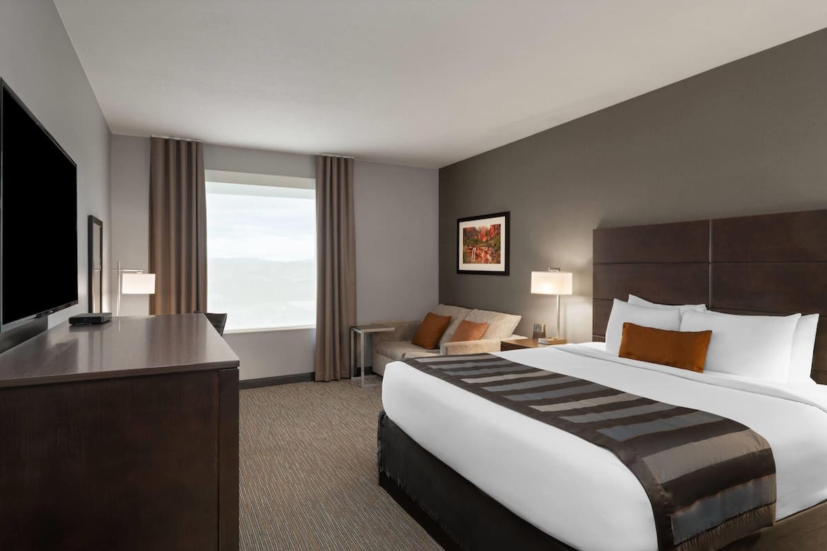 A hotel room with a large bed, a desk, a TV, and a window with curtains.