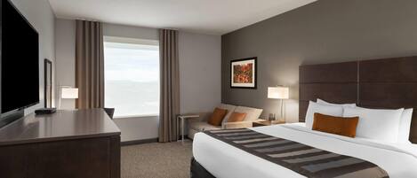 A hotel room with a large bed, a desk, a TV, and a window with curtains.
