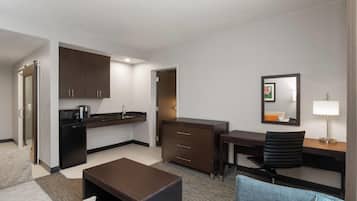Habitación de hotel compacta con kitchenette, escritorio, silla, sofá y una pequeña mesa.