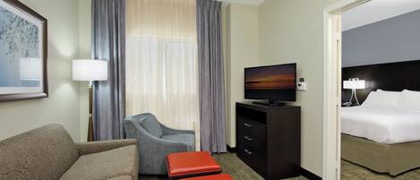 A hotel room with a sofa, armchair, ottoman, television, and a bed.