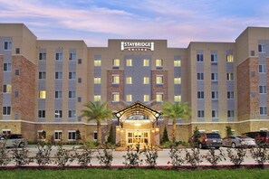 A Staybridge Suites hotel with a central entrance, multiple floors, and a parking lot. - Staybridge Suites Houston - Medical Center by IHG (Houston)
