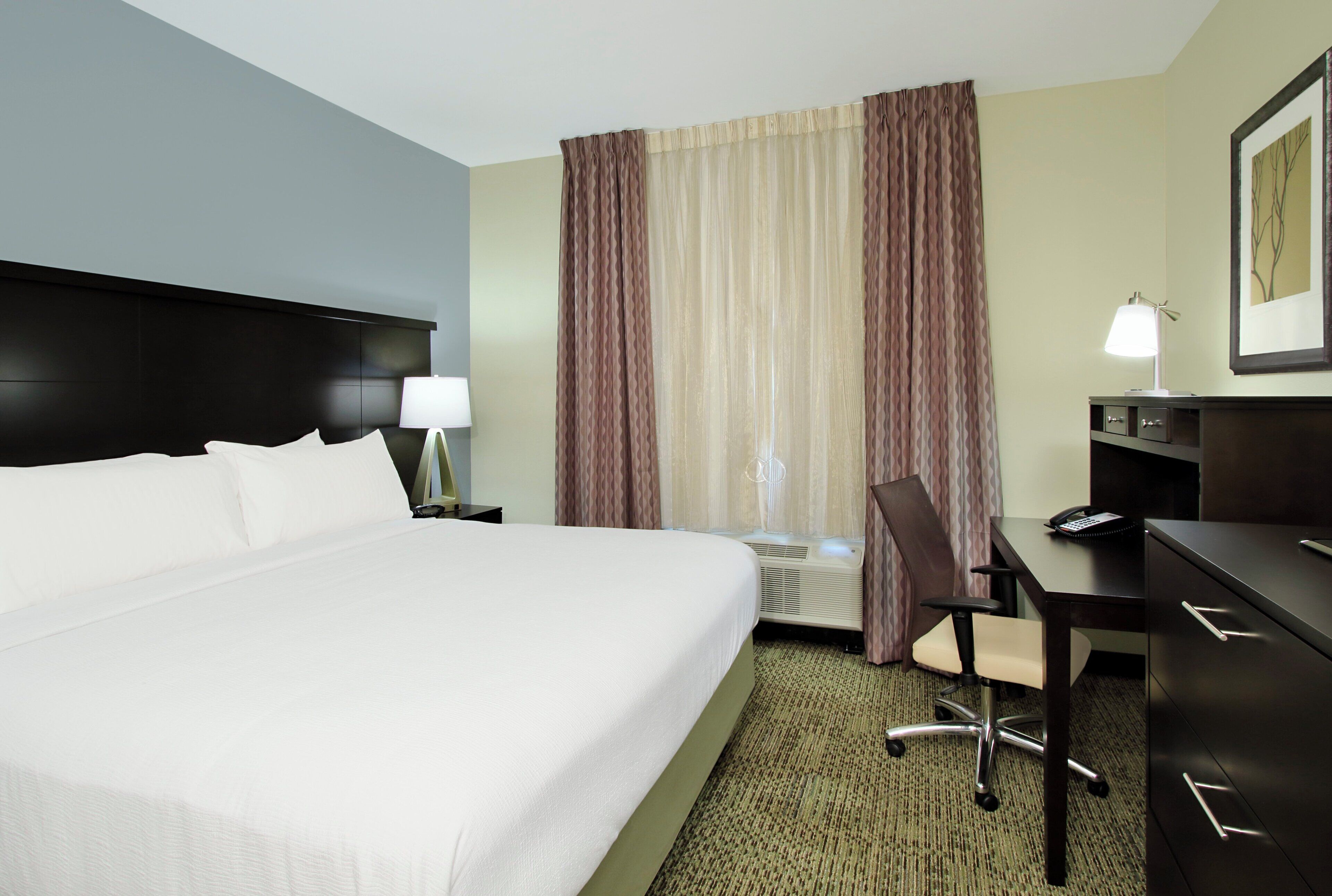 A hotel room with a large bed, a desk with a chair, a lamp, and a telephone.