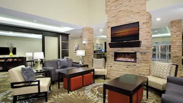A hotel lobby with a fireplace, seating area, and a flat-screen TV mounted on a stone wall.