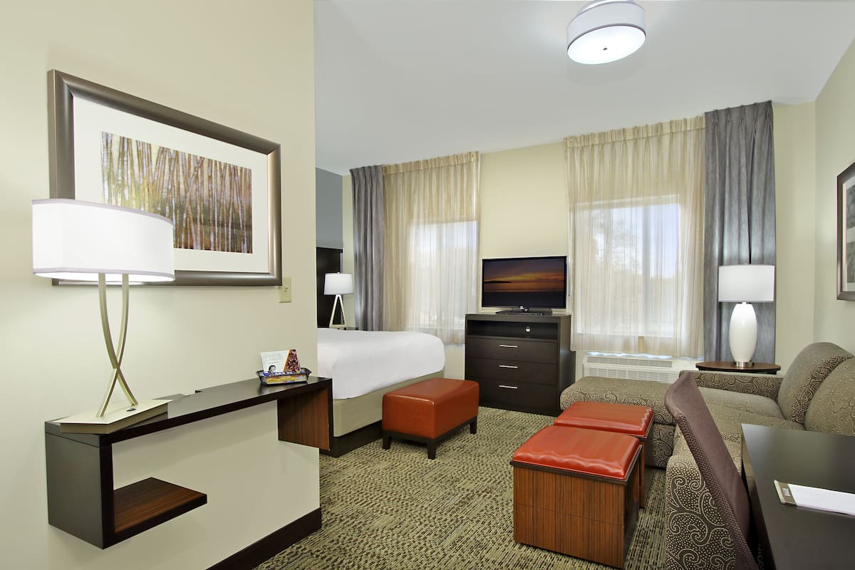 A hotel room with a bed, a desk, a television, a sofa, and a carpeted floor.